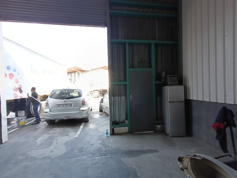 Industrial garage space featuring a large roller shutter door, concrete flooring, and metal wall cladding, suitable for vehicle maintenance or storage.