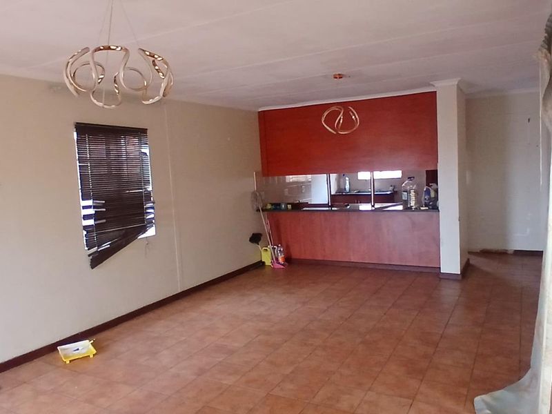 An open-plan living and kitchen area featuring tiled flooring, built-in cabinetry with a breakfast bar, and neutral wall finishes.