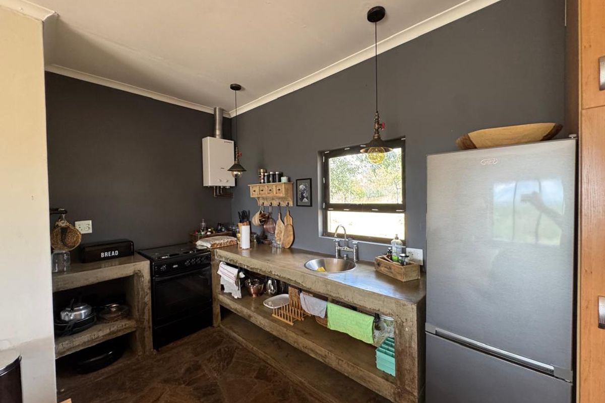 Rustic kitchen featuring concrete countertops, integrated shelving, a gas stove, and a stainless steel sink, set against dark grey walls.
