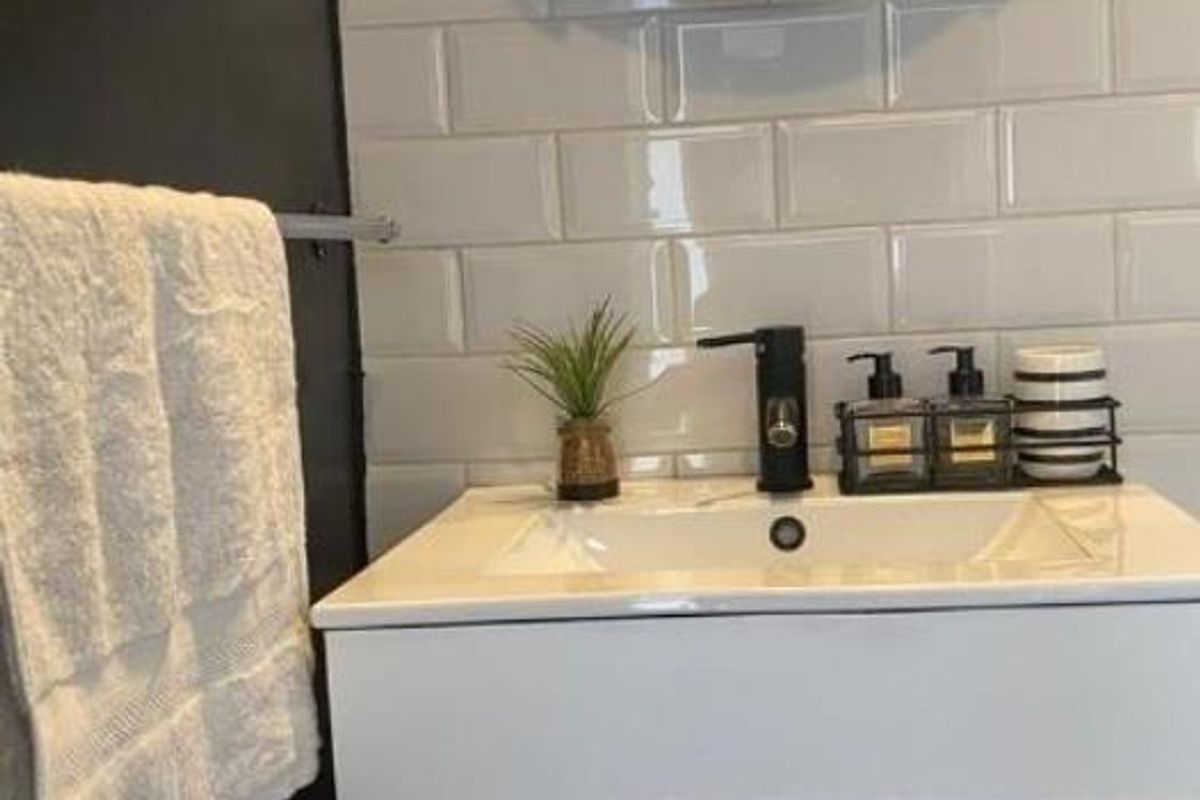 Modern bathroom vanity featuring a white basin, matte black faucet, and white subway tile backsplash with a circular wooden-framed mirror.