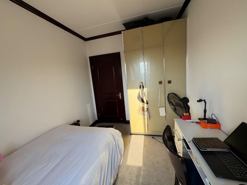 A functional bedroom featuring carpeted flooring, a built-in wardrobe with glossy finish, and dark timber door detailing.