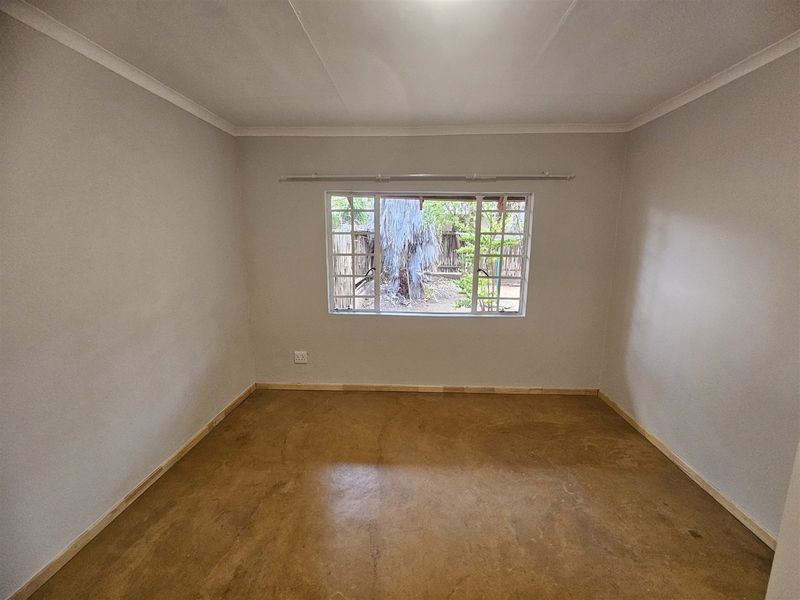 A clean, empty bedroom featuring a polished concrete floor, neutral walls, and a window overlooking the garden area.
