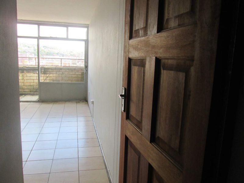 A vacant hallway featuring tiled flooring and a wooden door, leading to a balcony with an exterior view.