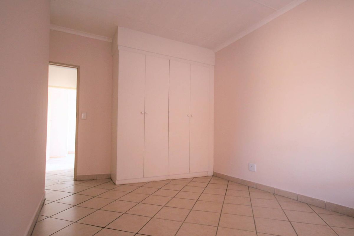 A clean, empty bedroom featuring neutral walls, tiled flooring, and a built-in wardrobe, offering a blank canvas for personalization.