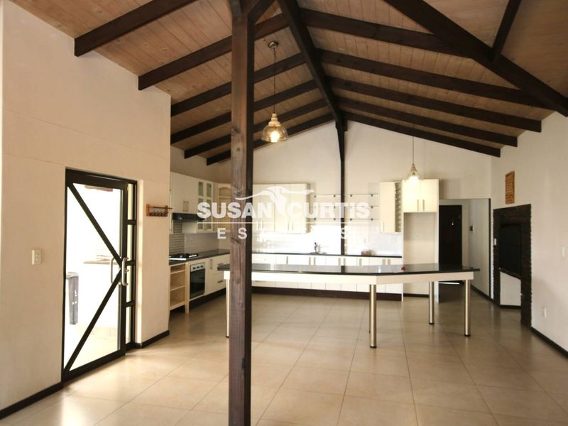 Spacious open-plan kitchen and living area featuring high vaulted ceilings with exposed timber beams, tiled flooring, and a central kitchen island.