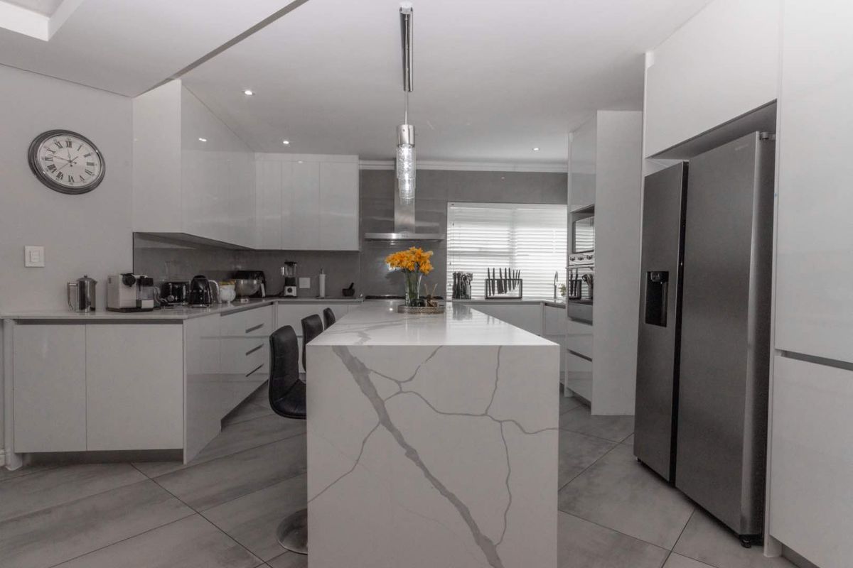 Modern kitchen featuring a large stone-topped island, sleek white cabinetry, built-in appliances, and contemporary tiled flooring.