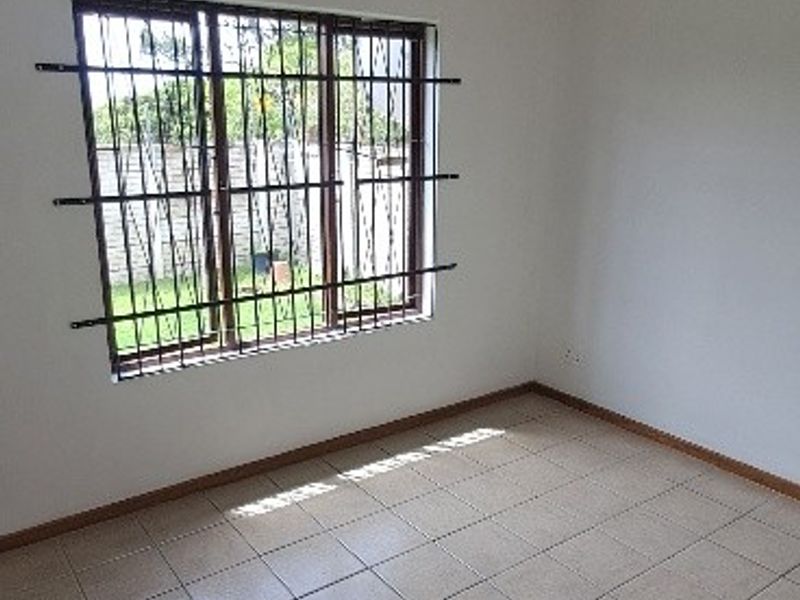 A clean, empty bedroom featuring neutral tiled flooring and a window fitted with security bars, offering a blank canvas for personalization.