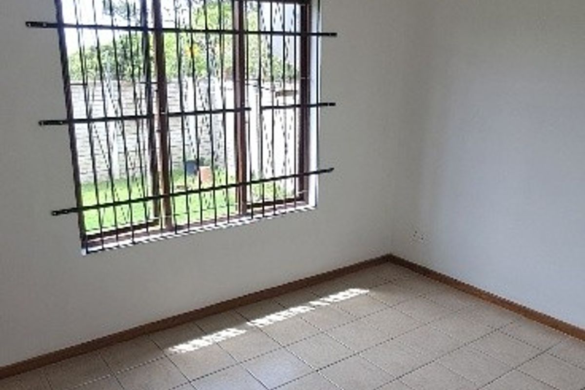 A clean, empty bedroom featuring neutral tiled flooring and a window fitted with security bars, offering a blank canvas for personalization.