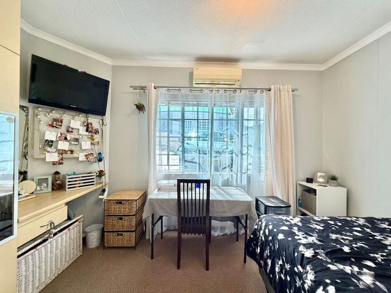 A functional bedroom featuring carpeted flooring, a built-in desk area, and a wall-mounted split-system air conditioner unit.