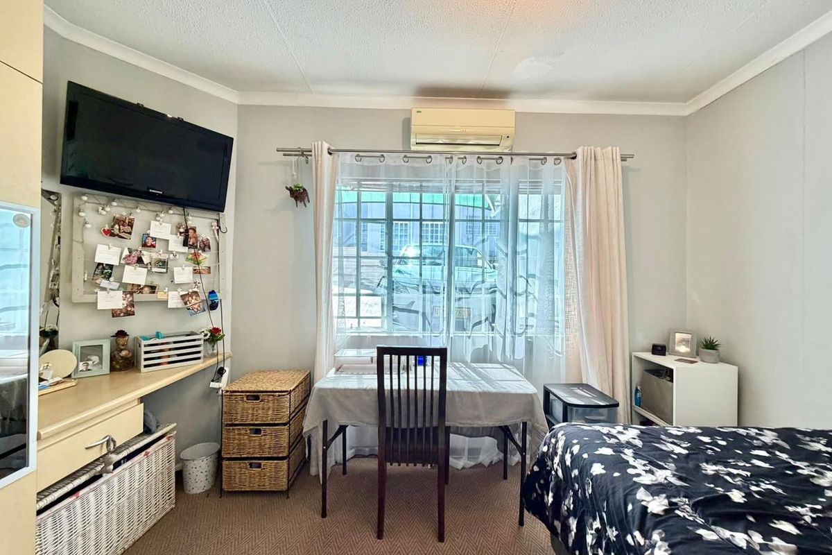 A functional bedroom featuring carpeted flooring, a built-in desk area, and a wall-mounted split-system air conditioner unit.