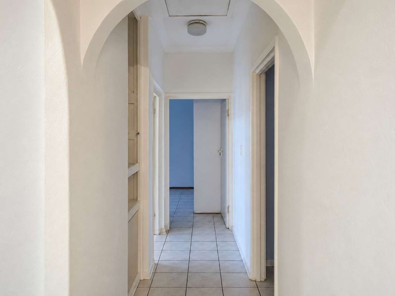 A bright, empty hallway featuring a decorative archway, tiled flooring, and built-in shelving, providing access to multiple rooms.