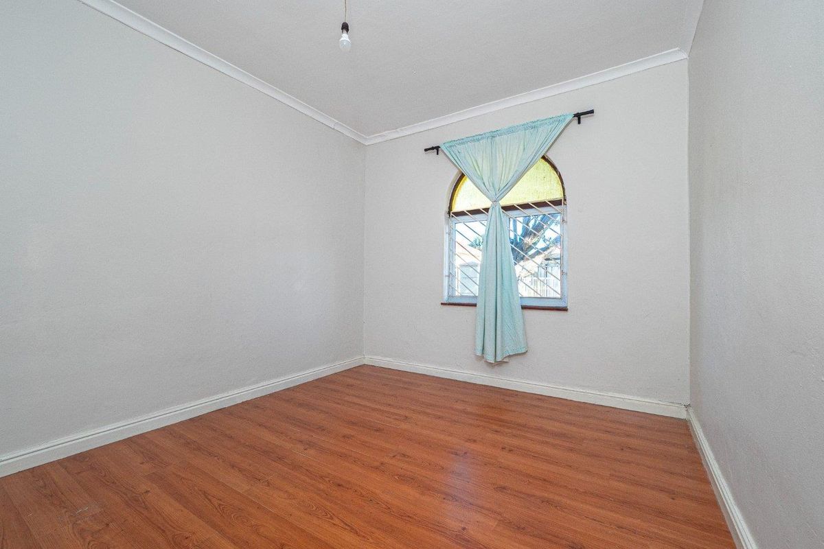 An empty bedroom featuring laminate flooring, coving, and an arched window with security bars.