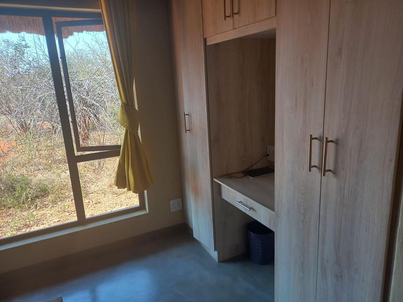 A bedroom featuring light wood built-in cupboards and a matching integrated desk, with a large window overlooking the natural landscape.