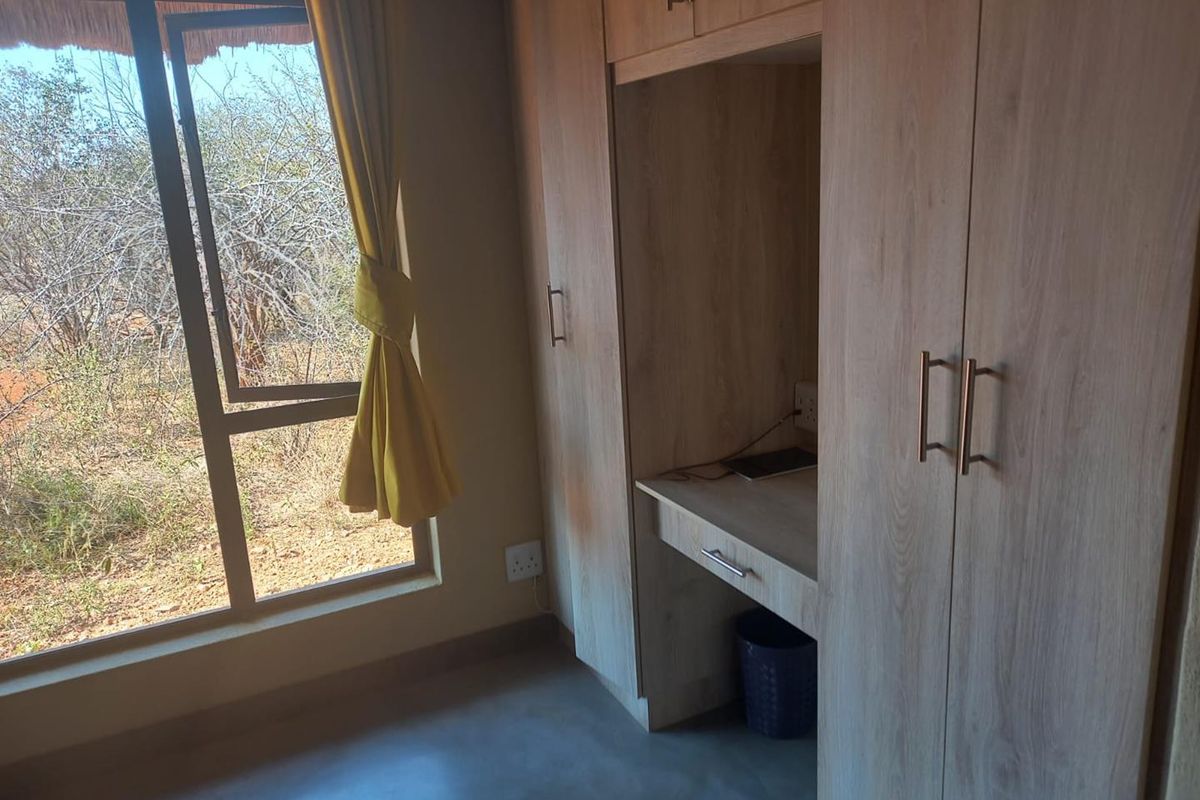 A bedroom featuring light wood built-in cupboards and a matching integrated desk, with a large window overlooking the natural landscape.