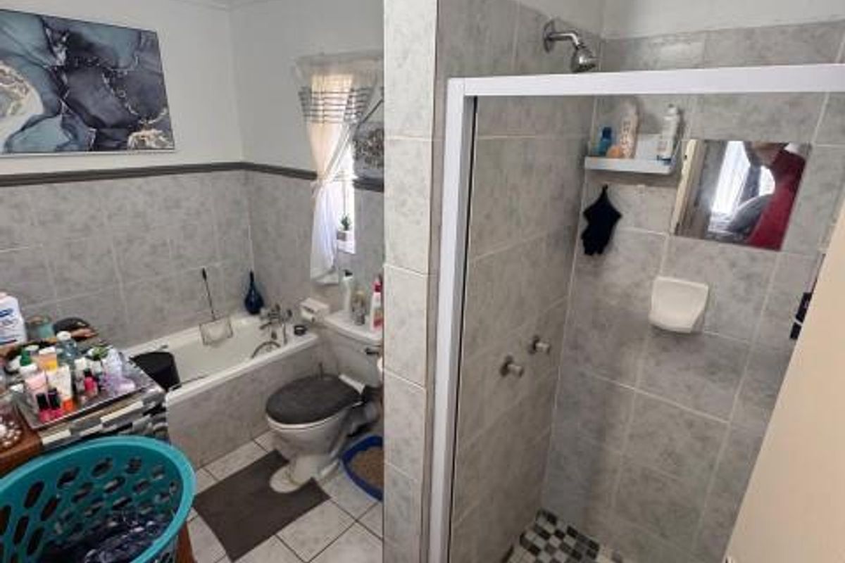 A functional bathroom featuring a separate shower enclosure with mosaic floor tiles, a bathtub, and a toilet with neutral wall tiling.