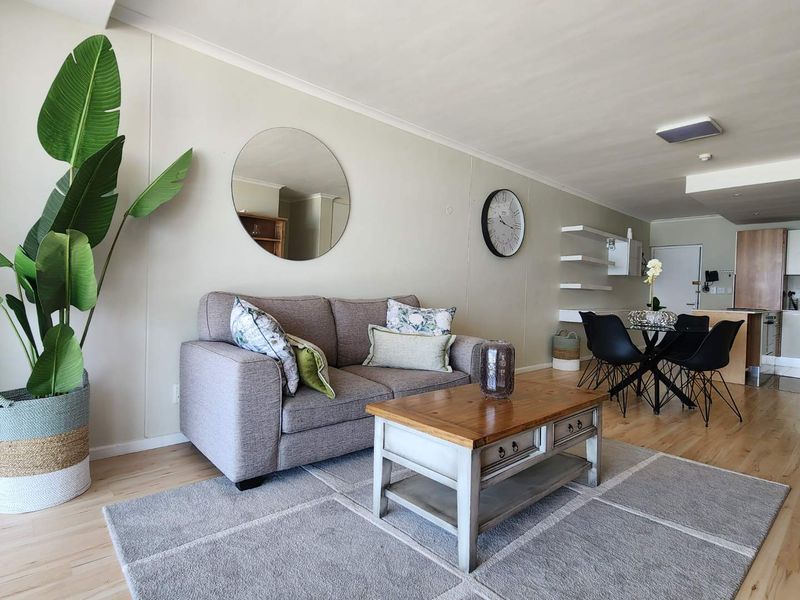 An open-plan living and dining area featuring light laminate flooring, neutral walls, and integrated kitchen cabinetry in the background.