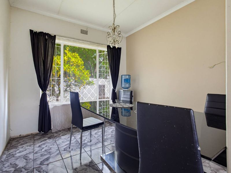 Dining room featuring tiled flooring, a large window with security bars, and a central pendant light fixture. Requires minor finishing touches like skirting boards.