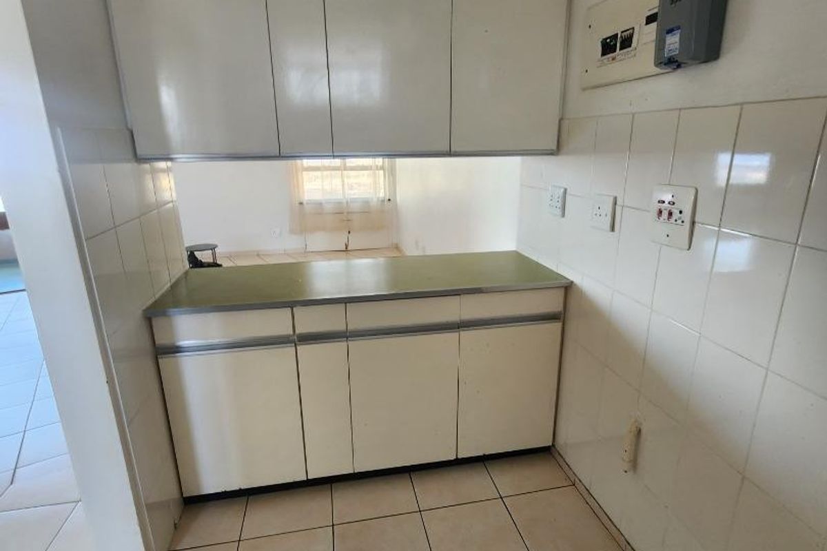 A compact, empty kitchen area featuring dated built-in cabinetry, tiled backsplash, and tiled flooring, offering a blank canvas for renovation.