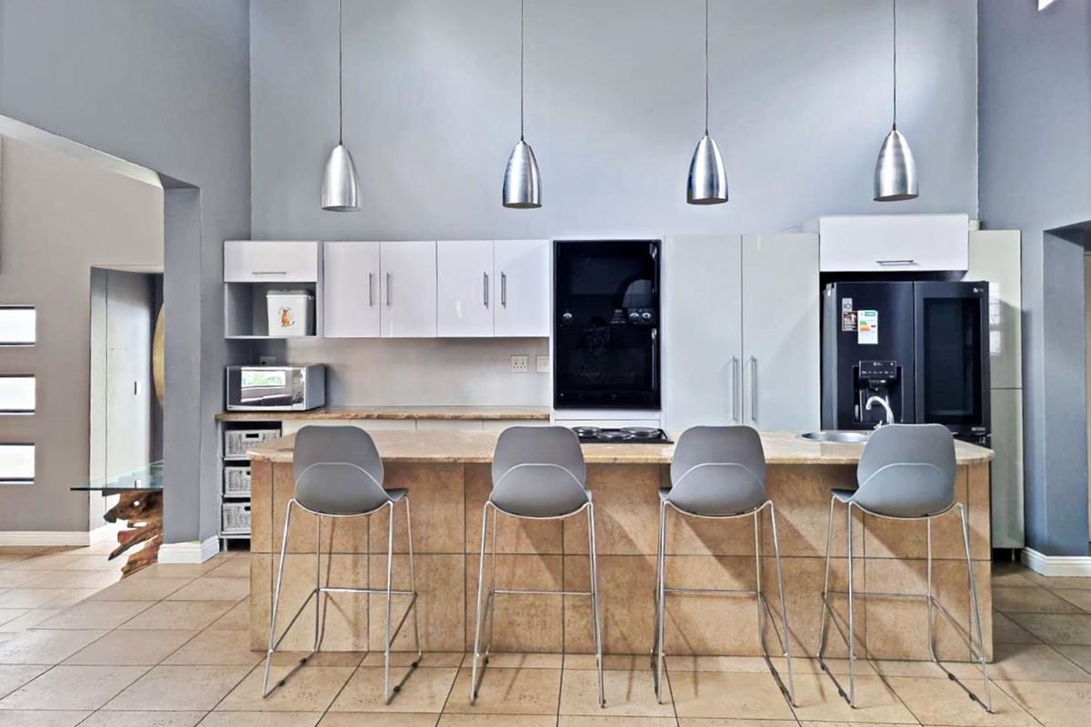 Modern kitchen featuring a large stone island with breakfast bar seating, built-in oven, electric hob, and sleek cabinetry under high ceilings.