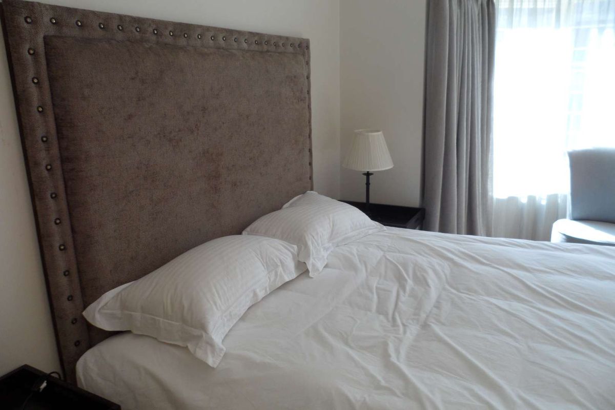 A bedroom featuring a large upholstered headboard and window with curtains.