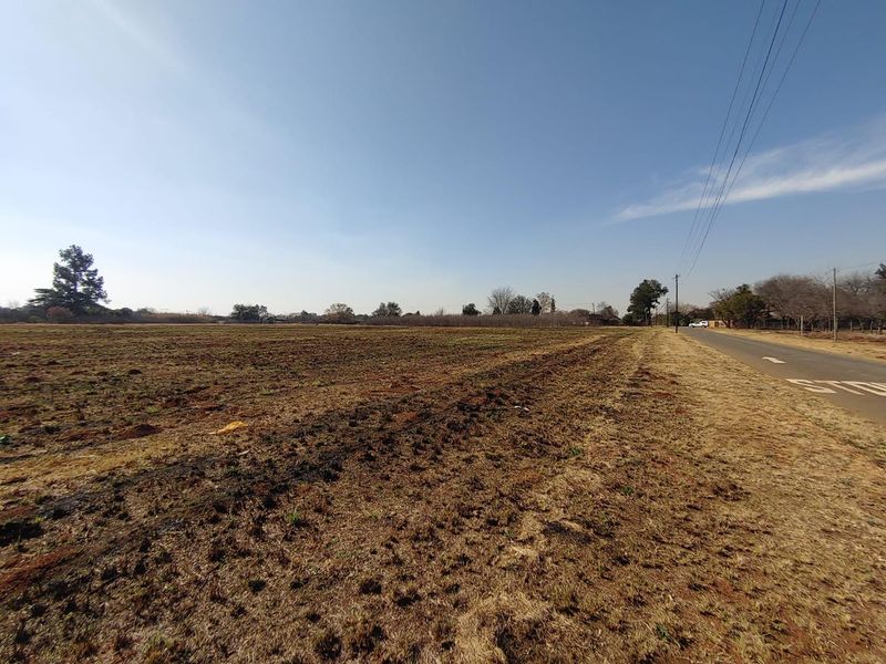 A wide-angle view of a vacant commercial land plot adjacent to a paved road with visible utility infrastructure.