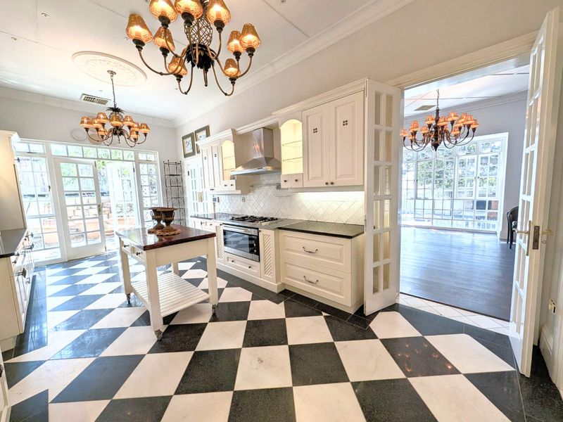 Elegant kitchen featuring classic checkerboard marble flooring, custom white cabinetry, stone countertops, and high-end built-in appliances, opening into a bright adjacent living space.