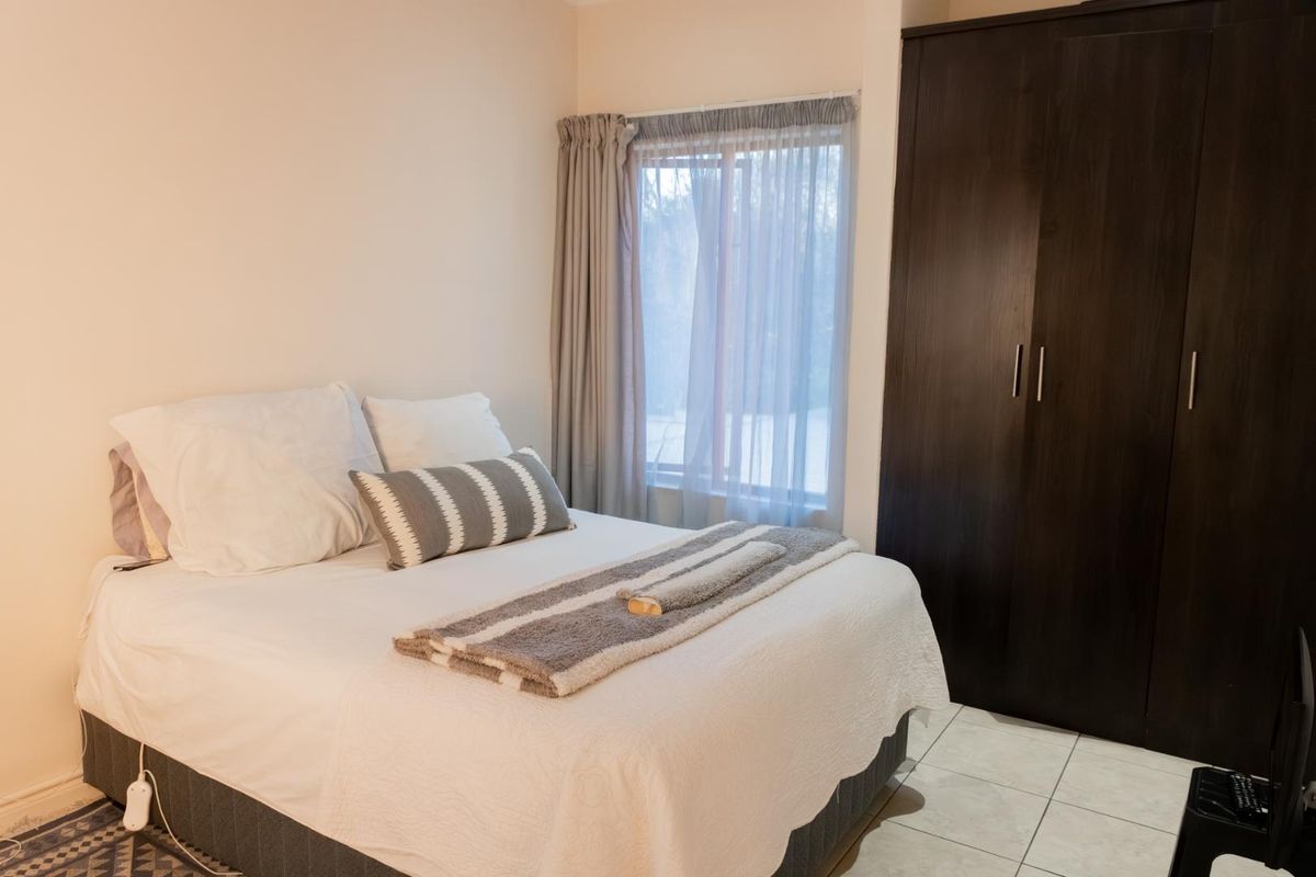 A bedroom featuring tiled flooring and a built-in dark wood wardrobe, providing functional storage space.