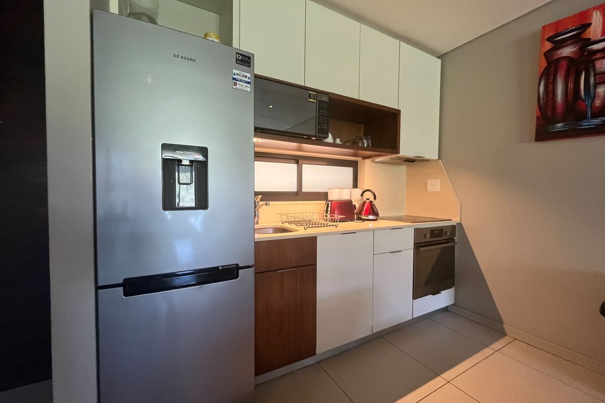 A compact, modern kitchen featuring sleek two-tone cabinetry, integrated appliances including an oven and hob, and under-cabinet lighting for a functional workspace.