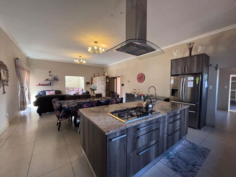 Spacious open-plan living area featuring a modern kitchen island with gas hob, extractor fan, and ample cabinetry, flowing into the dining and lounge space.