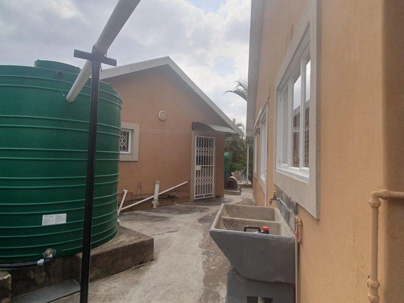 Rear exterior area featuring a large water storage tank, concrete utility sink, and paved walkway alongside the building structure.
