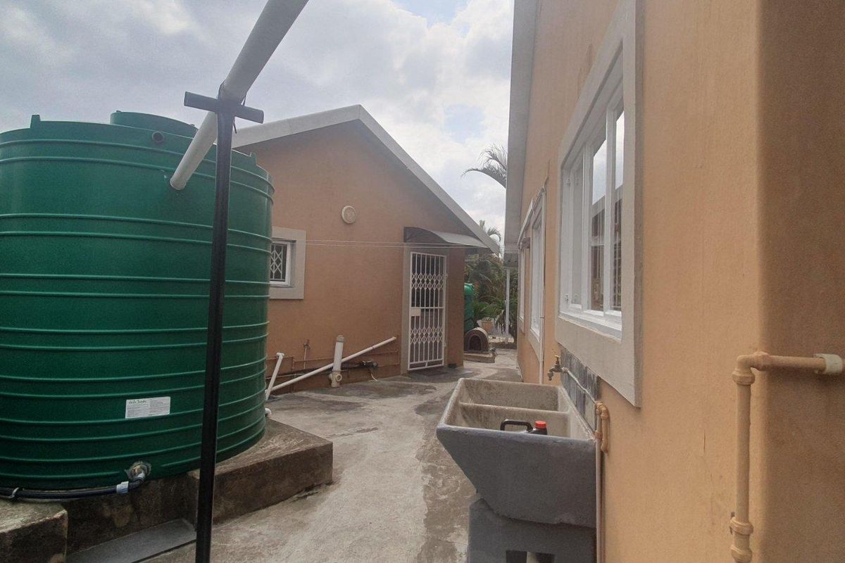 Rear exterior area featuring a large water storage tank, concrete utility sink, and paved walkway alongside the building structure.