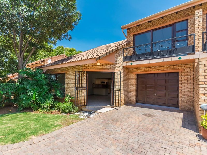 Front view of a face brick townhouse featuring a paved driveway, single garage, and an upper-level balcony with metal railings.