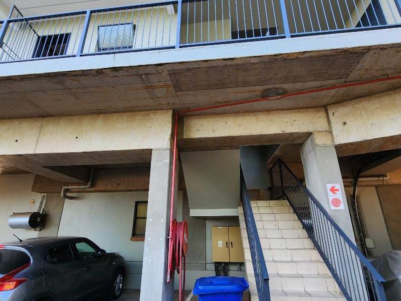 Exterior view of an apartment building showing a concrete staircase, covered parking area, and metal safety railings.
