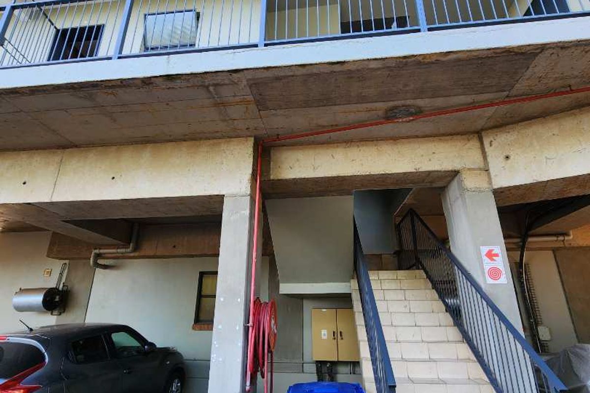 Exterior view of an apartment building showing a concrete staircase, covered parking area, and metal safety railings.