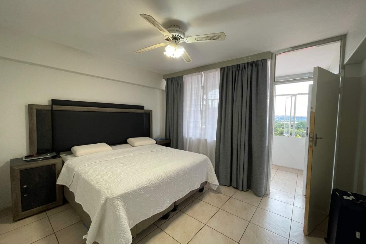 A bedroom featuring tiled flooring, a ceiling fan, and direct access to a private balcony through a glass door.