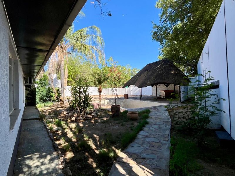 Rear garden area featuring a swimming pool, a traditional thatch lapa, and a stone paved pathway leading through the yard.