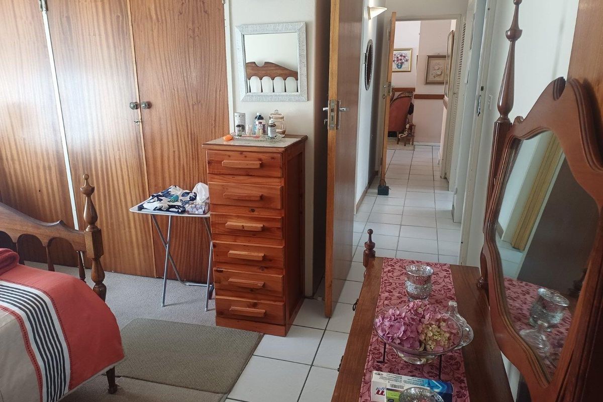 A bedroom featuring built-in wooden cupboards and tiled flooring, with an adjacent hallway leading to other areas of the home.