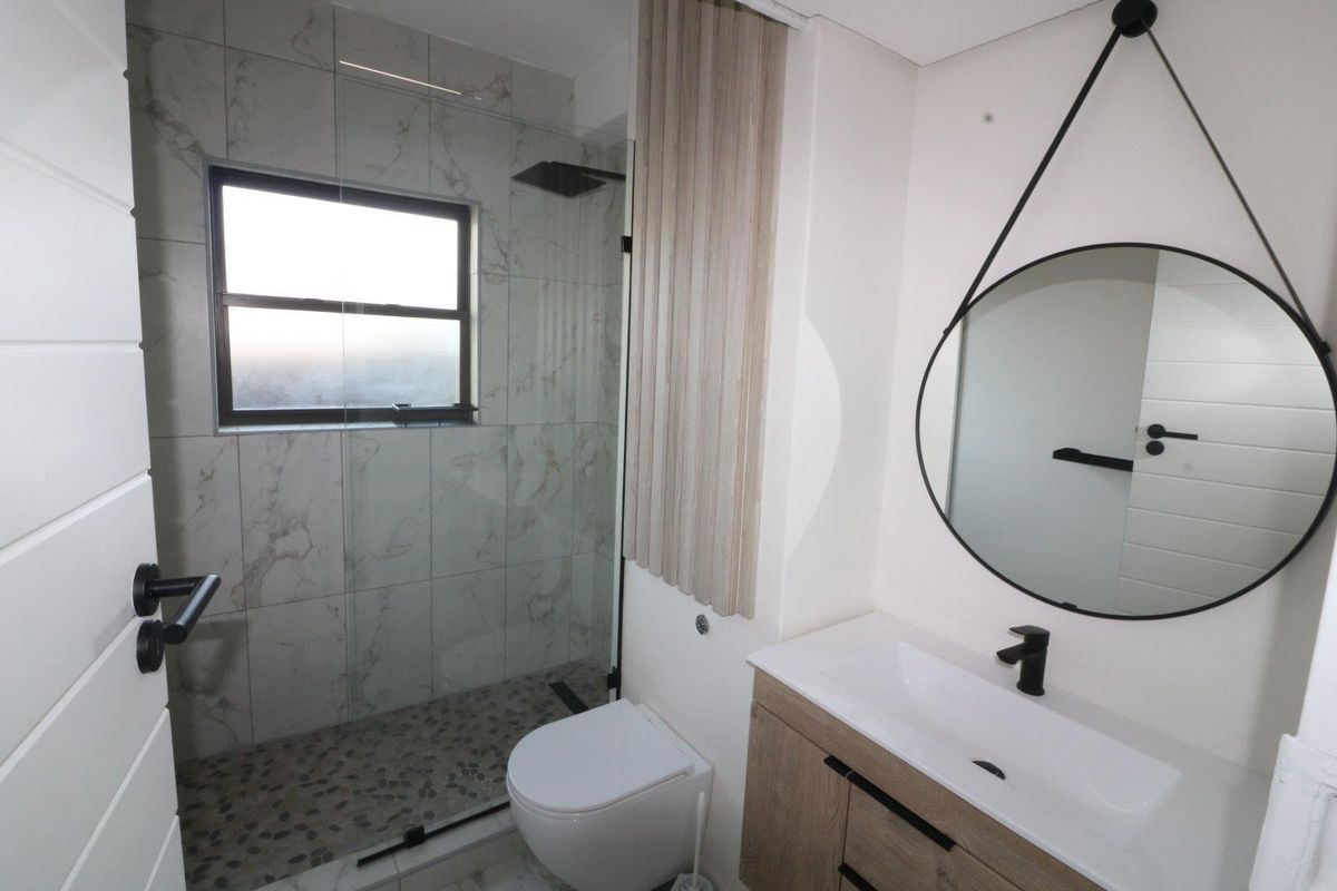 Modern bathroom featuring a walk-in shower with rain head, wall-hung toilet, and a contemporary vanity with black fixtures and marble-look tiling.
