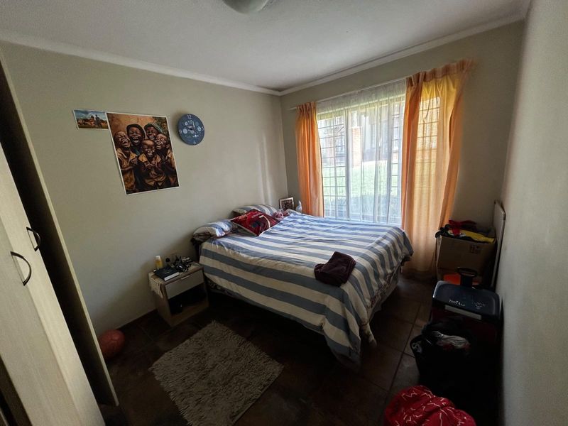 A functional bedroom featuring tiled flooring, a built-in wardrobe, and a window fitted with security bars for added peace of mind.