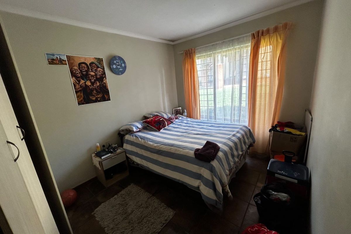 A functional bedroom featuring tiled flooring, a built-in wardrobe, and a window fitted with security bars for added peace of mind.