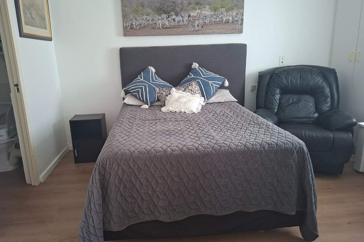 A bedroom featuring light wood-look flooring and built-in wardrobe storage, with an adjacent view into a bathroom area.