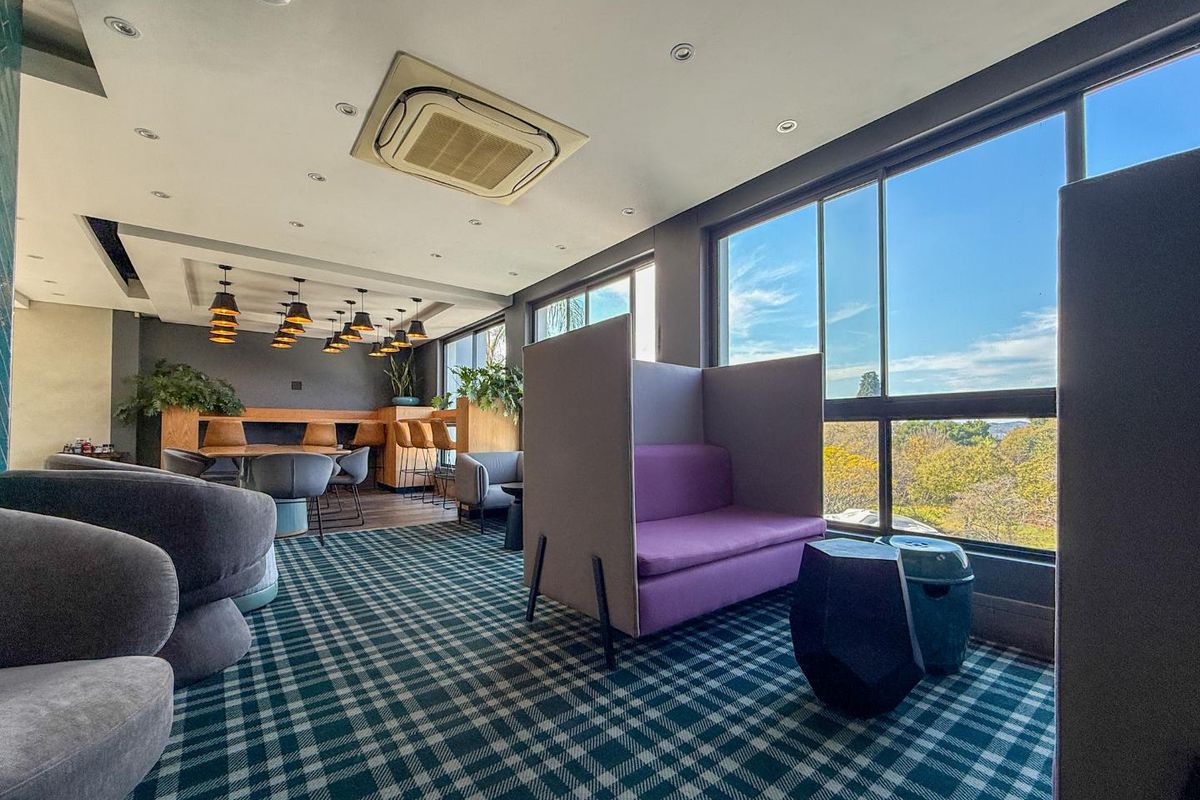 A modern, well-lit communal living area featuring large windows with scenic views, recessed ceiling lighting, and integrated air conditioning.