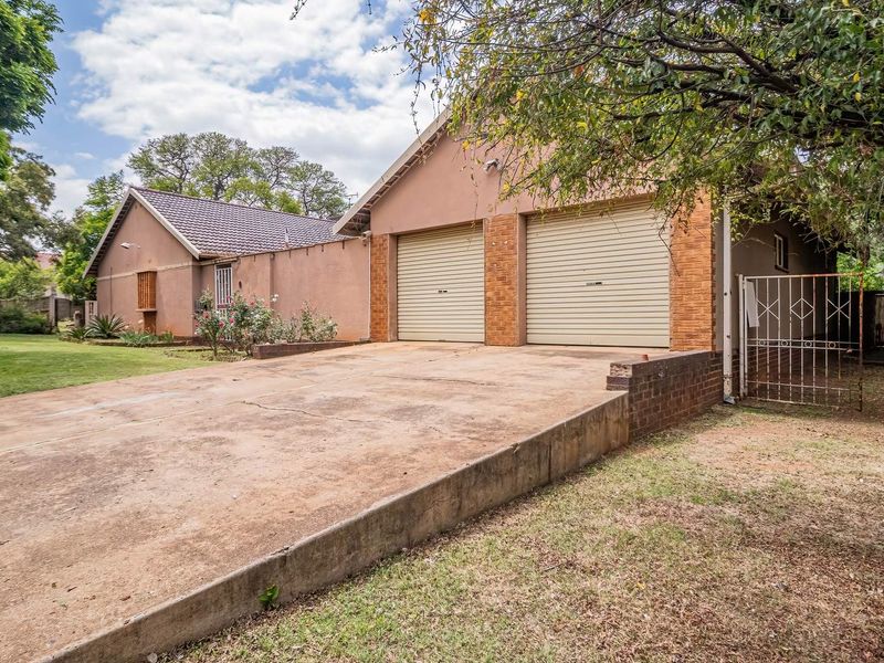 Front view of the property featuring a double garage, concrete driveway, and established garden area with a secure metal gate entrance.