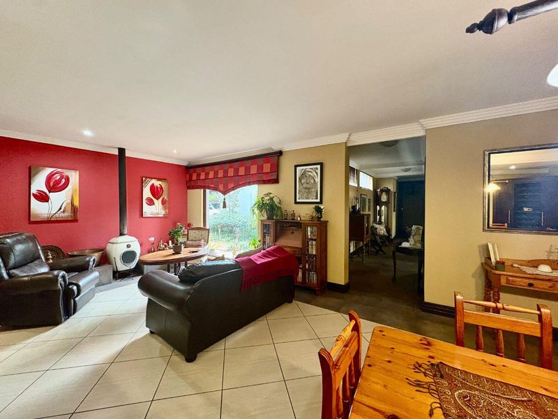 Spacious living room featuring tiled flooring, a freestanding fireplace, and a bold red accent wall, leading into an adjacent hallway area.