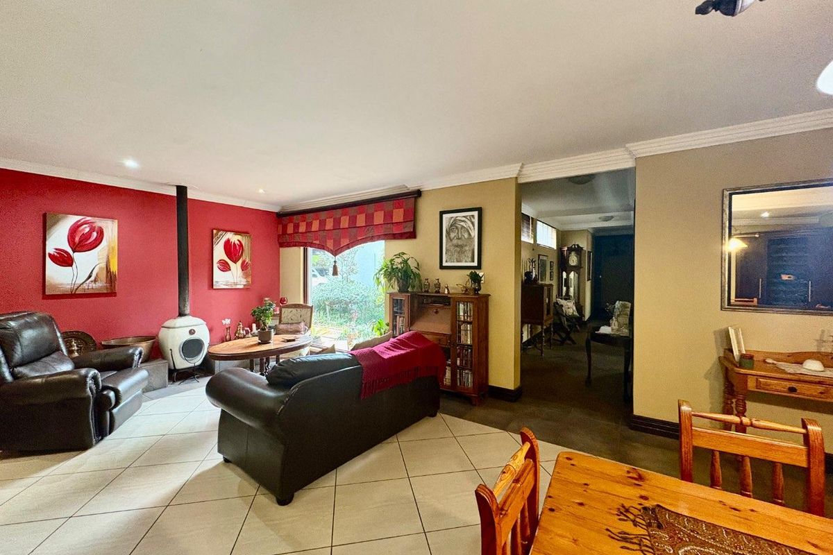 Spacious living room featuring tiled flooring, a freestanding fireplace, and a bold red accent wall, leading into an adjacent hallway area.
