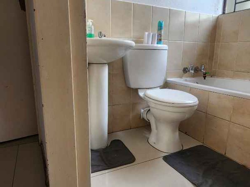A functional bathroom featuring a pedestal basin, toilet, and bathtub with neutral ceramic tiling throughout.