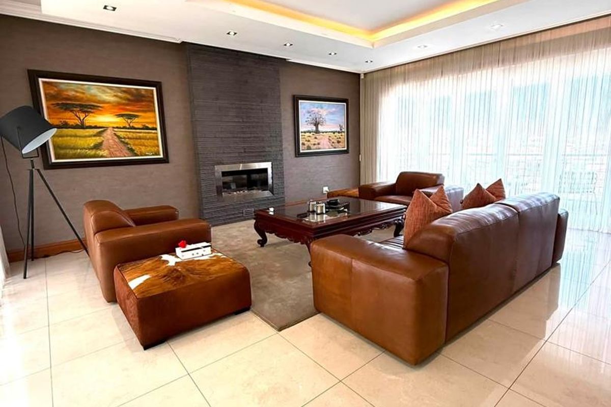 Spacious living room featuring a modern stone-clad fireplace, recessed ceiling with ambient cove lighting, and polished tiled flooring.