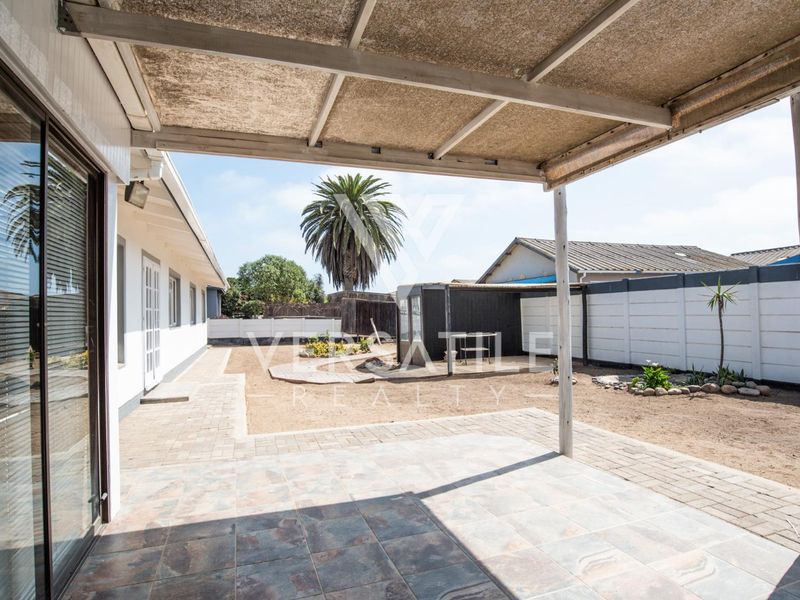 A covered patio area with tiled flooring, leading out to a spacious backyard with perimeter walling and established garden features.