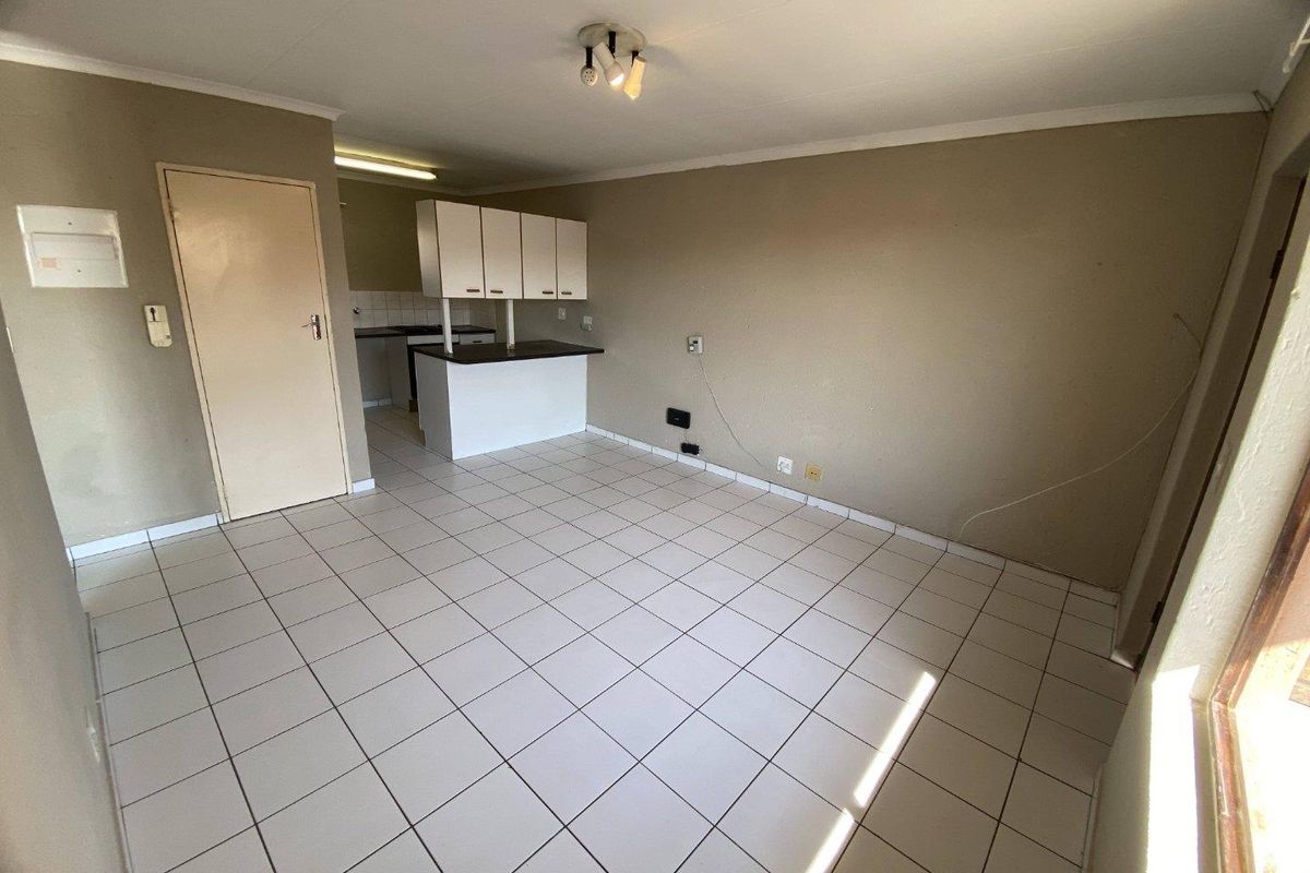 An empty open-plan living and kitchen area featuring tiled flooring, neutral wall tones, and basic built-in kitchen cabinetry.