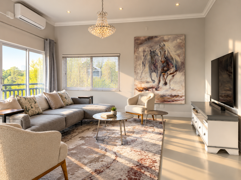 A bright and well-maintained living room featuring a split-system air conditioner, elegant crystal chandelier, and large sliding glass doors leading to an outdoor area.